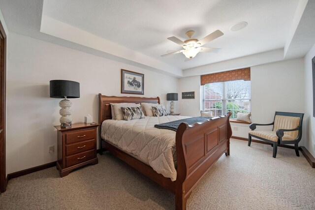 bedroom with light colored carpet, baseboards, and a tray ceiling