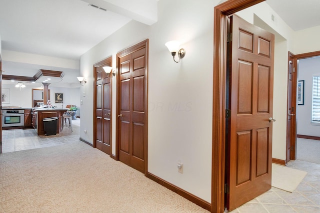 hallway with visible vents, light colored carpet, and baseboards