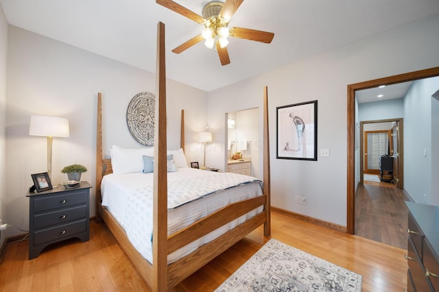 bedroom featuring light wood-style flooring, a ceiling fan, ensuite bathroom, baseboards, and a wood stove