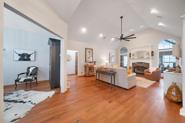 living area featuring high vaulted ceiling, light wood-style flooring, a ceiling fan, a premium fireplace, and baseboards