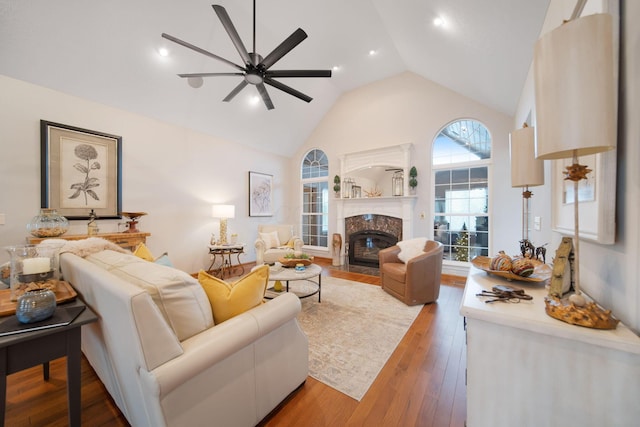living area featuring high vaulted ceiling, ceiling fan, a fireplace, and hardwood / wood-style flooring