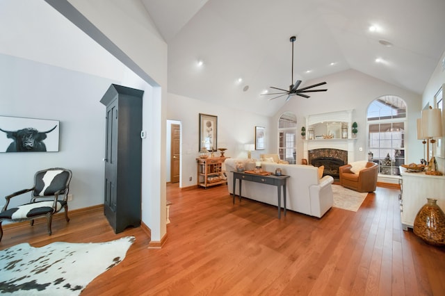 living area with light wood finished floors, baseboards, ceiling fan, a premium fireplace, and high vaulted ceiling
