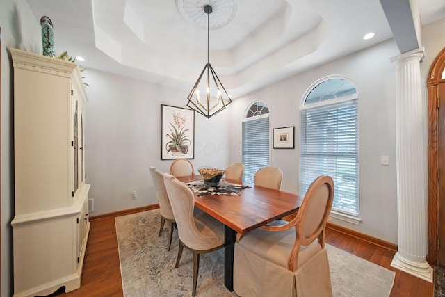 dining area with a tray ceiling, decorative columns, and dark wood-style floors