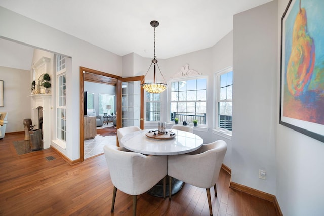 dining area with visible vents, wood-type flooring, an inviting chandelier, a fireplace, and baseboards