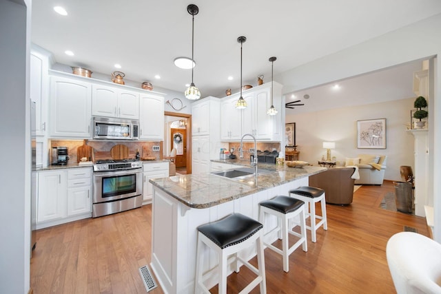 kitchen featuring visible vents, a breakfast bar, a sink, appliances with stainless steel finishes, and light stone countertops