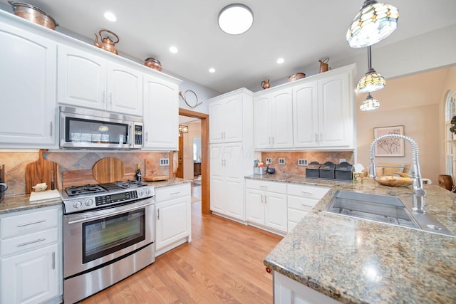 kitchen featuring light wood finished floors, pendant lighting, stainless steel appliances, white cabinetry, and a sink