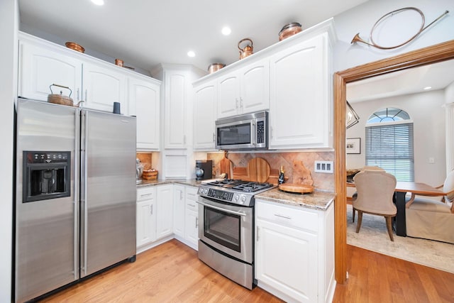 kitchen featuring light stone countertops, white cabinetry, appliances with stainless steel finishes, and light wood finished floors