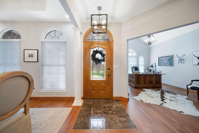entryway featuring decorative columns, baseboards, wood finished floors, and a chandelier