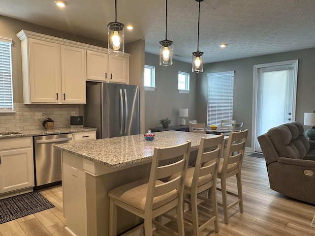 kitchen featuring tasteful backsplash, a center island, white cabinetry, light wood-style floors, and appliances with stainless steel finishes