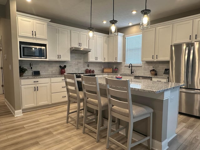 kitchen with under cabinet range hood, appliances with stainless steel finishes, white cabinets, and a sink