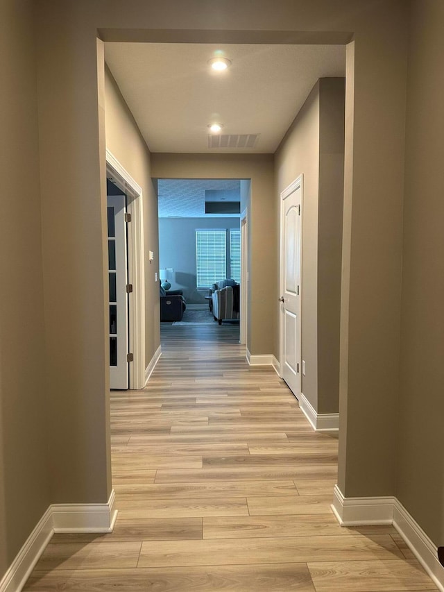 hallway with visible vents, baseboards, and light wood-type flooring