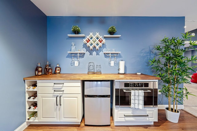 bar with light wood-style floors, baseboards, a bar, and appliances with stainless steel finishes