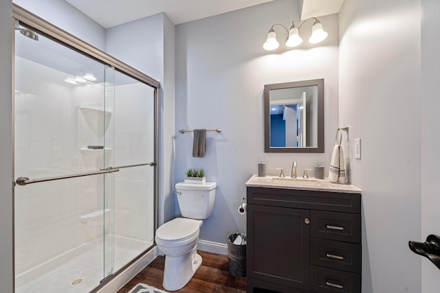 bathroom with toilet, wood finished floors, a shower stall, baseboards, and vanity