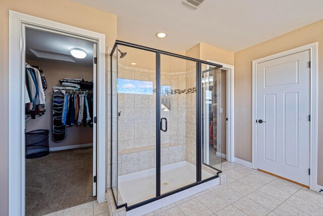 bathroom featuring tile patterned floors, a spacious closet, baseboards, and a stall shower