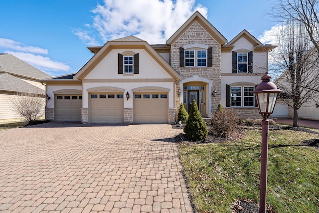 french country style house featuring stone siding, stucco siding, an attached garage, and decorative driveway