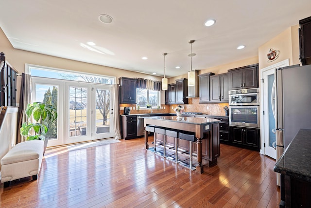 kitchen featuring dark wood finished floors, appliances with stainless steel finishes, a kitchen bar, wall chimney range hood, and a center island