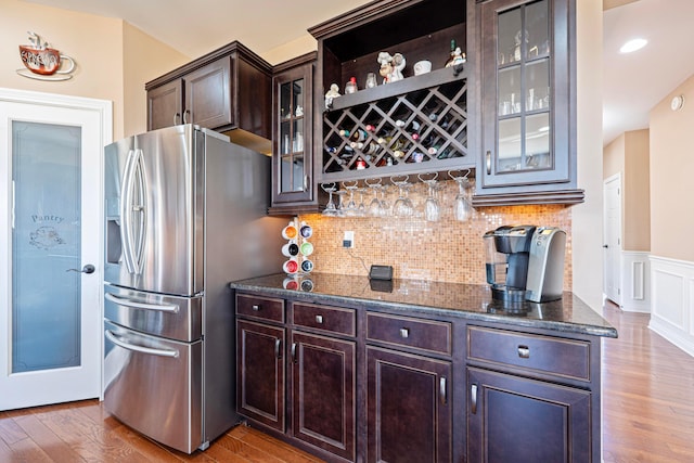 kitchen with dark stone counters, light wood-style flooring, dark brown cabinetry, stainless steel refrigerator with ice dispenser, and tasteful backsplash