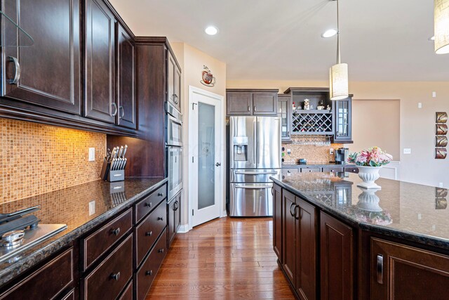 kitchen featuring dark wood finished floors, dark stone counters, stainless steel fridge, and dark brown cabinetry