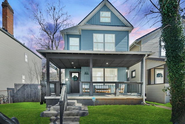 view of front facade with covered porch, board and batten siding, a front lawn, and fence