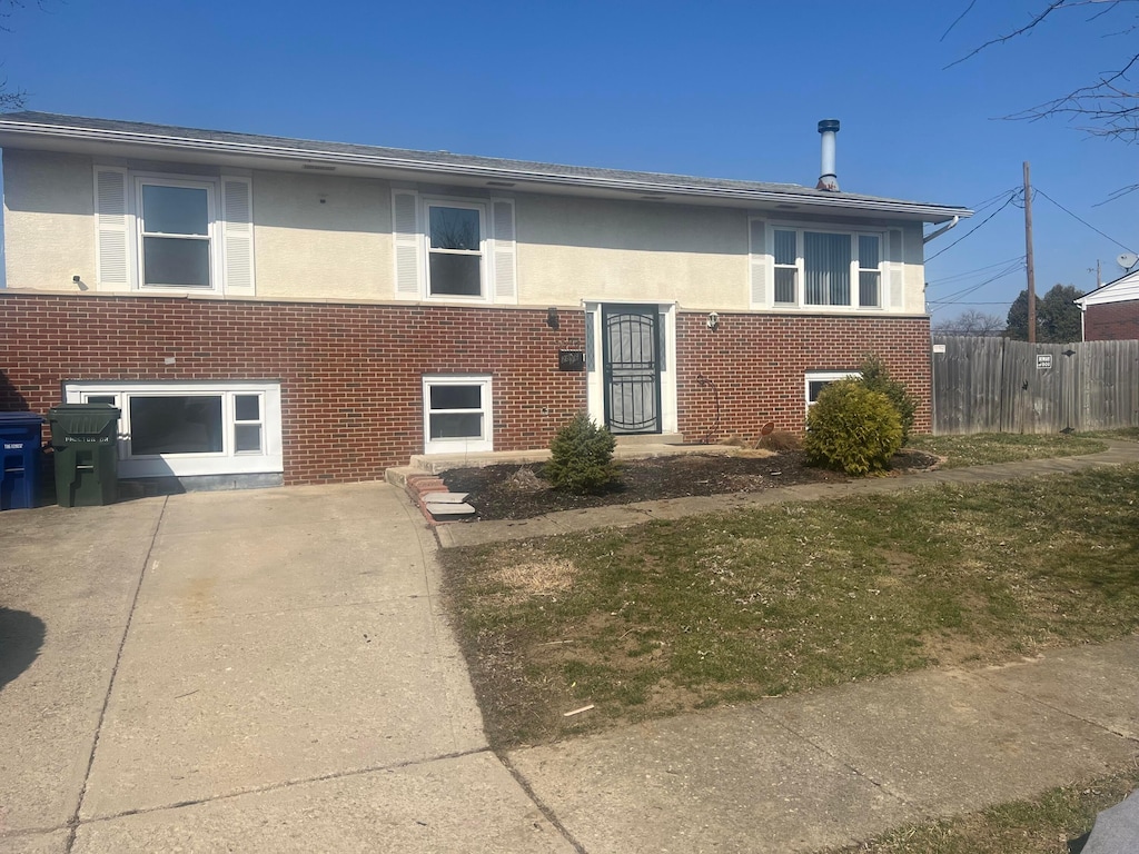 bi-level home featuring stucco siding, brick siding, concrete driveway, and fence