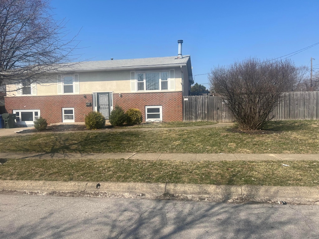 view of side of home with a yard, fence, brick siding, and stucco siding