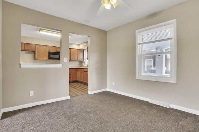 unfurnished living room with carpet flooring, baseboards, a ceiling fan, and a sink