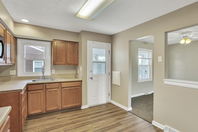 kitchen featuring a sink, brown cabinetry, light countertops, wood finished floors, and a textured ceiling