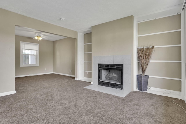 unfurnished living room featuring carpet, a tiled fireplace, a ceiling fan, baseboards, and built in features
