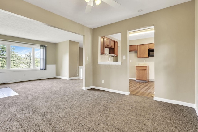 unfurnished living room with carpet flooring, a ceiling fan, and baseboards
