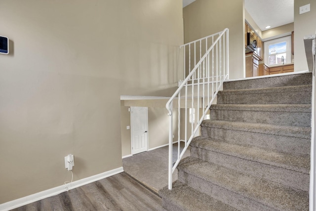 staircase with baseboards, wood finished floors, and a towering ceiling