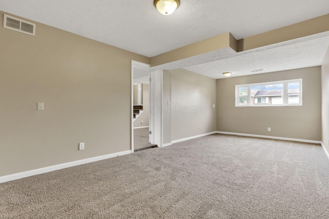 empty room with a textured ceiling, carpet flooring, stairs, and baseboards