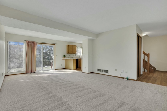 unfurnished living room featuring stairway, light colored carpet, visible vents, and baseboards