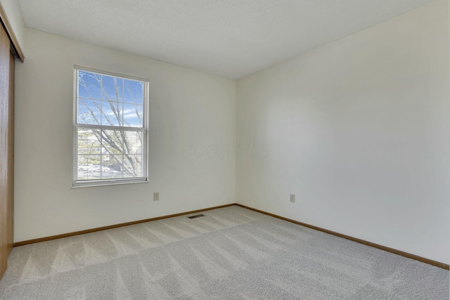 empty room with visible vents, light carpet, and baseboards