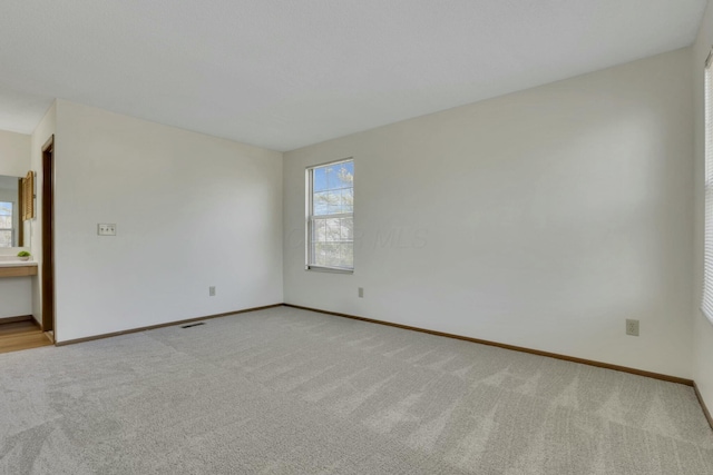 spare room with baseboards and light colored carpet