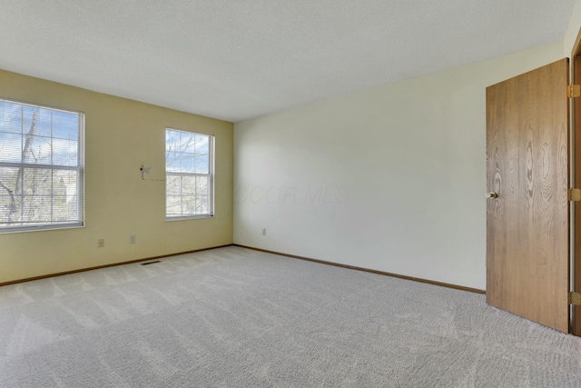 unfurnished room featuring light carpet, visible vents, a textured ceiling, and baseboards