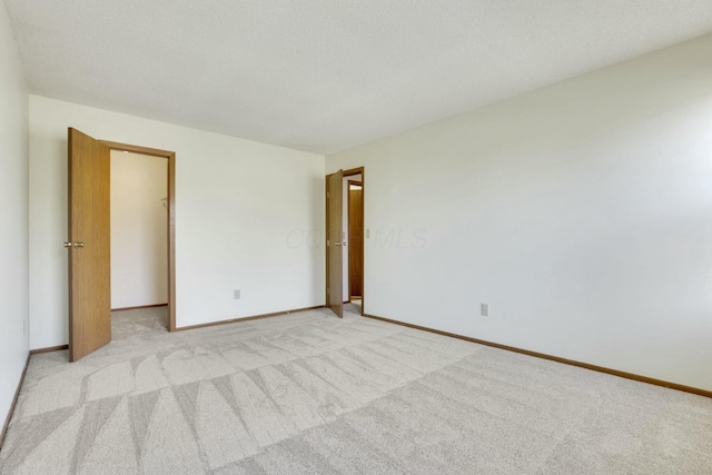 spare room featuring light colored carpet, baseboards, and a textured ceiling