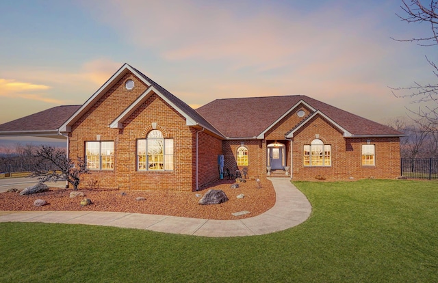 ranch-style house with a yard, fence, brick siding, and roof with shingles