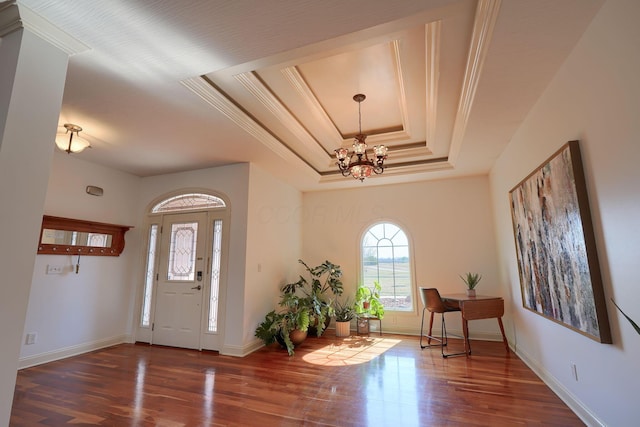 entrance foyer featuring wood finished floors, baseboards, ornamental molding, a raised ceiling, and a chandelier