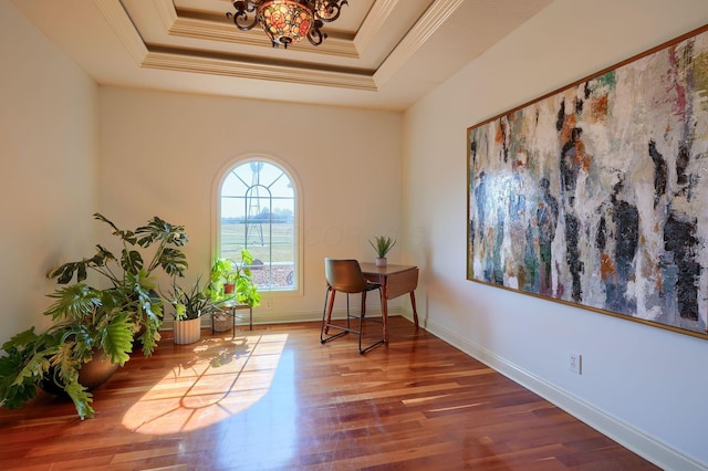 living area featuring a tray ceiling, baseboards, wood finished floors, and crown molding