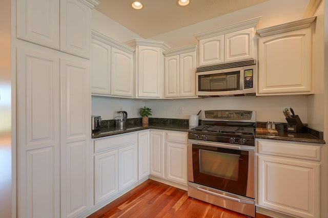 kitchen with dark stone countertops, wood finished floors, recessed lighting, stainless steel appliances, and white cabinetry