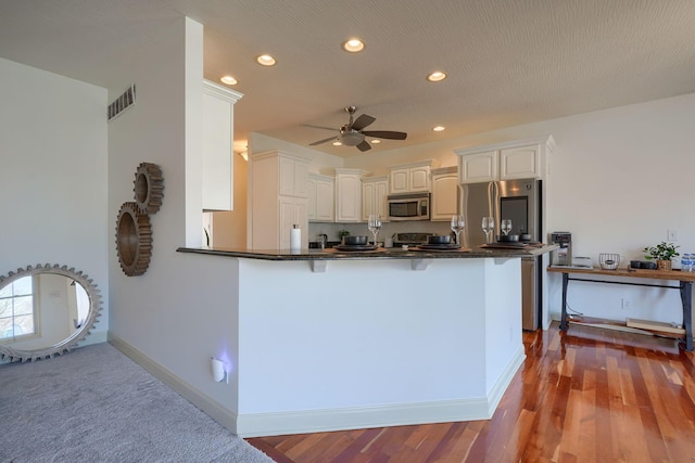 kitchen featuring dark countertops, visible vents, a breakfast bar area, appliances with stainless steel finishes, and a peninsula