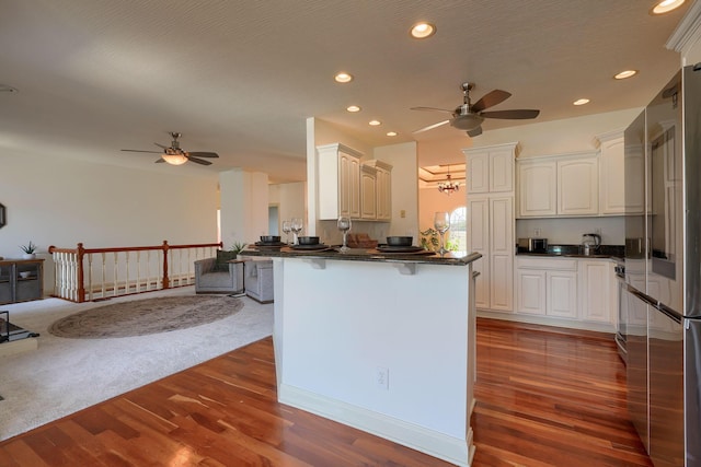 kitchen featuring dark countertops, a peninsula, ceiling fan, and stainless steel refrigerator