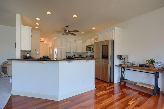 kitchen with dark countertops, a peninsula, a kitchen breakfast bar, stainless steel appliances, and a ceiling fan