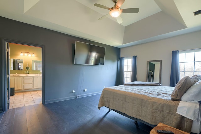 bedroom featuring ensuite bath, a raised ceiling, light wood-style floors, and baseboards