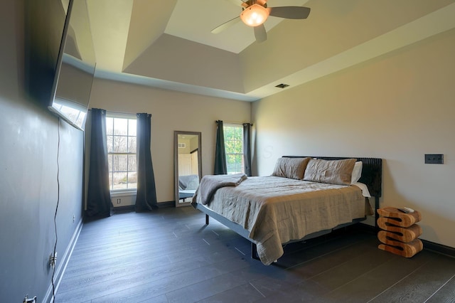 bedroom with a ceiling fan, visible vents, baseboards, a tray ceiling, and dark wood-type flooring