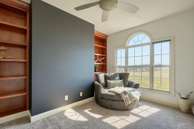 living area featuring built in features, carpet flooring, baseboards, and ceiling fan