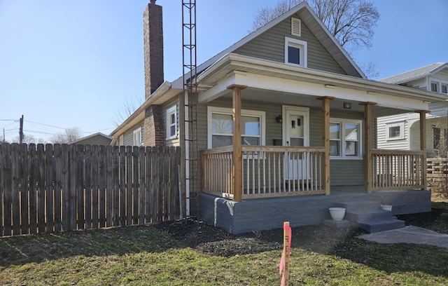 bungalow-style house featuring covered porch, a chimney, and fence