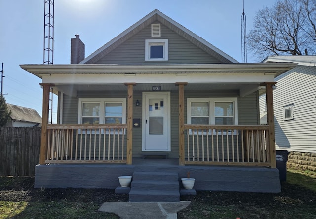 bungalow-style house with a porch, a chimney, and fence