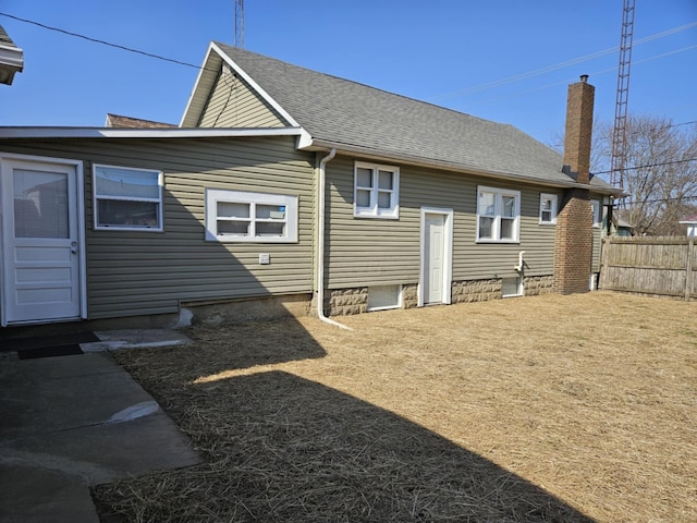 back of house with roof with shingles, a chimney, and fence