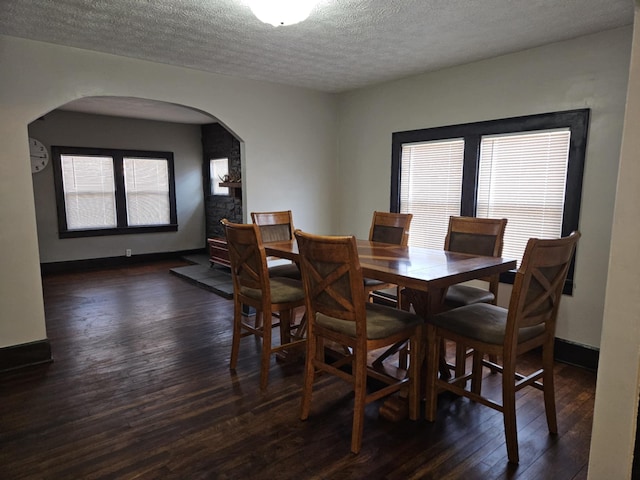 dining room featuring arched walkways, a textured ceiling, baseboards, and dark wood-style flooring